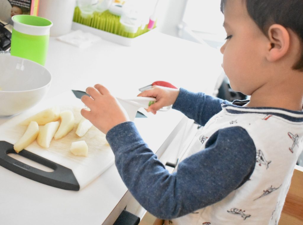 Toddler chopping baby food for brother, two under two